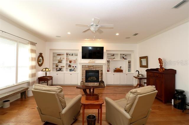 living area with visible vents, built in shelves, ornamental molding, a stone fireplace, and wood finished floors