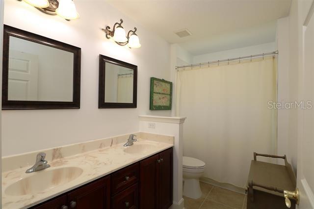 full bath featuring double vanity, tile patterned flooring, toilet, and a sink