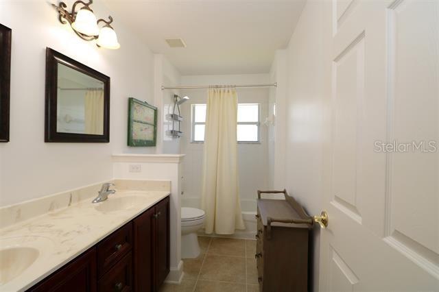 bathroom featuring visible vents, toilet, shower / tub combo with curtain, tile patterned floors, and a sink