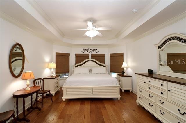 bedroom with a ceiling fan, dark wood-type flooring, a tray ceiling, and ornamental molding