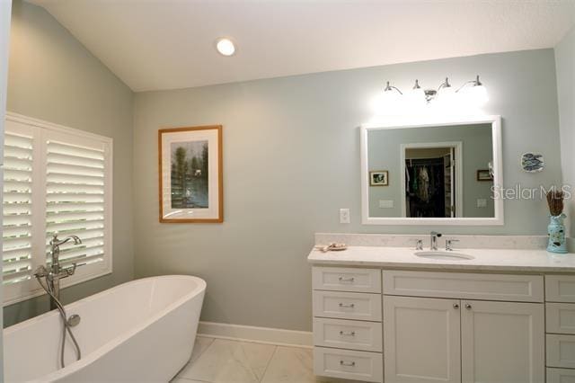 full bathroom featuring baseboards, a soaking tub, marble finish floor, and vanity