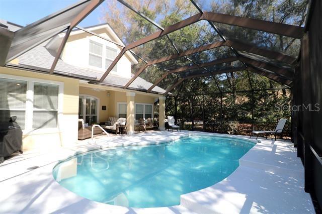 pool featuring glass enclosure, a patio, area for grilling, and an outdoor hangout area