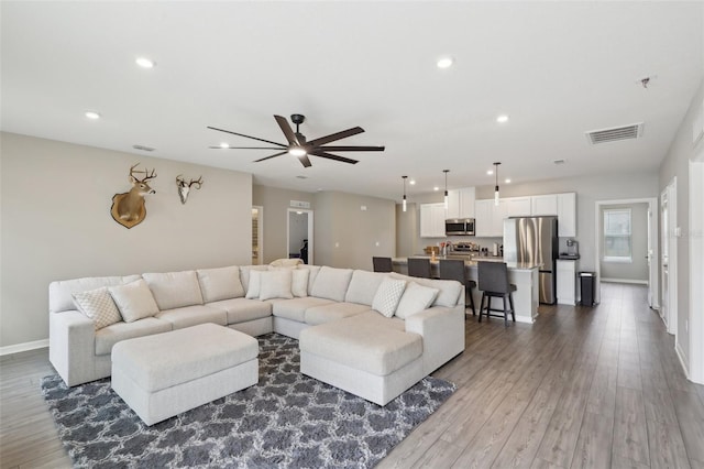 living room with recessed lighting, visible vents, baseboards, and wood finished floors