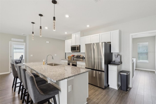 kitchen with a center island with sink, appliances with stainless steel finishes, wood finished floors, white cabinets, and a sink