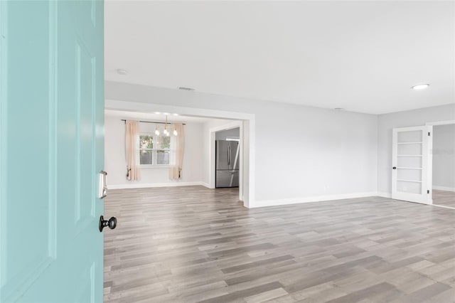 spare room featuring baseboards, a notable chandelier, and wood finished floors