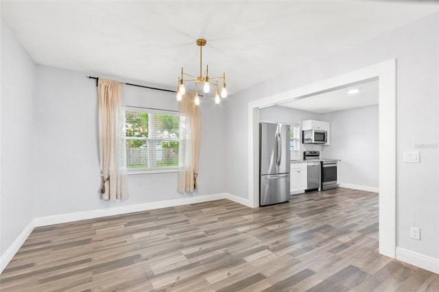 unfurnished dining area featuring baseboards, a notable chandelier, and wood finished floors