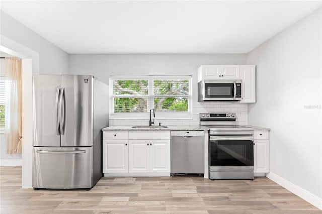 kitchen with light stone counters, a sink, decorative backsplash, stainless steel appliances, and a wealth of natural light