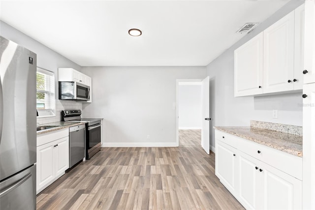 kitchen with light wood finished floors, visible vents, baseboards, decorative backsplash, and stainless steel appliances