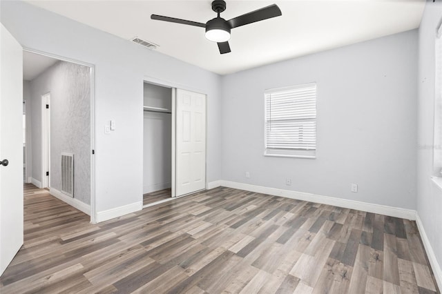 unfurnished bedroom with a closet, visible vents, baseboards, and wood finished floors