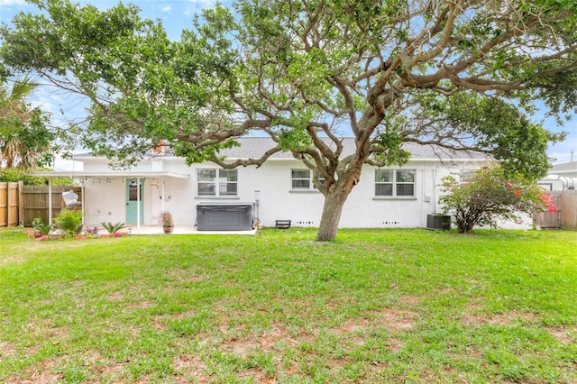 rear view of house with a yard, fence, and a hot tub