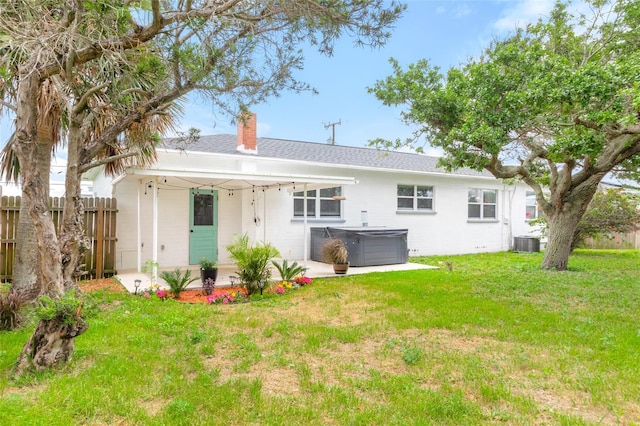 back of house with a hot tub, fence, a lawn, cooling unit, and a chimney