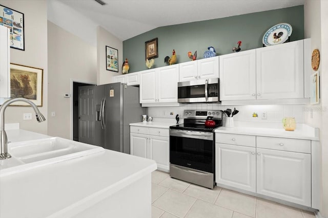 kitchen featuring light tile patterned flooring, stainless steel appliances, light countertops, white cabinets, and vaulted ceiling