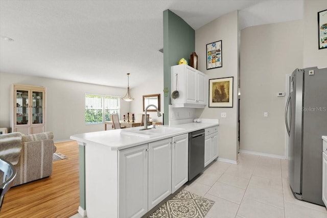 kitchen with light countertops, a peninsula, stainless steel appliances, white cabinetry, and a sink