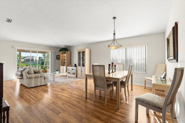 dining room featuring visible vents, a textured ceiling, baseboards, and wood finished floors