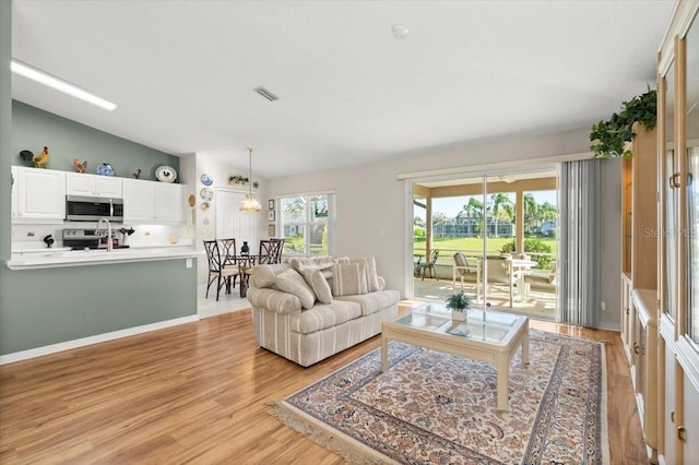 living area with baseboards, visible vents, an inviting chandelier, vaulted ceiling, and light wood-type flooring