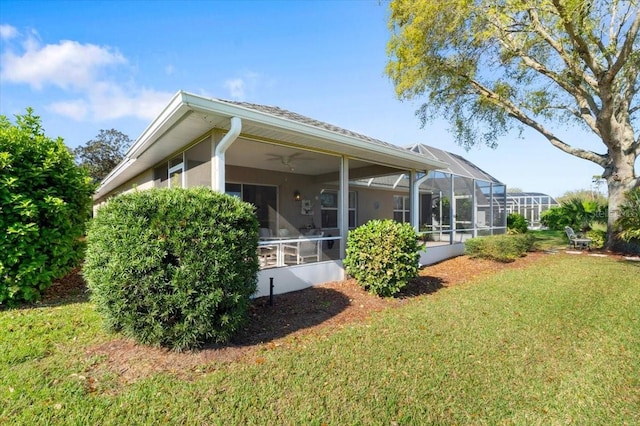 back of property featuring a yard, glass enclosure, a ceiling fan, and stucco siding