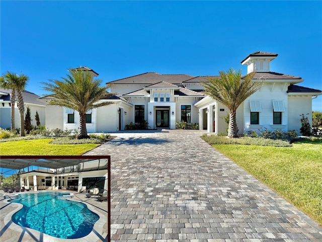 back of house with an outdoor pool, stucco siding, french doors, decorative driveway, and a lawn