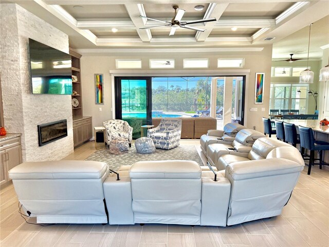 living room with ornamental molding, a stone fireplace, a high ceiling, coffered ceiling, and a ceiling fan