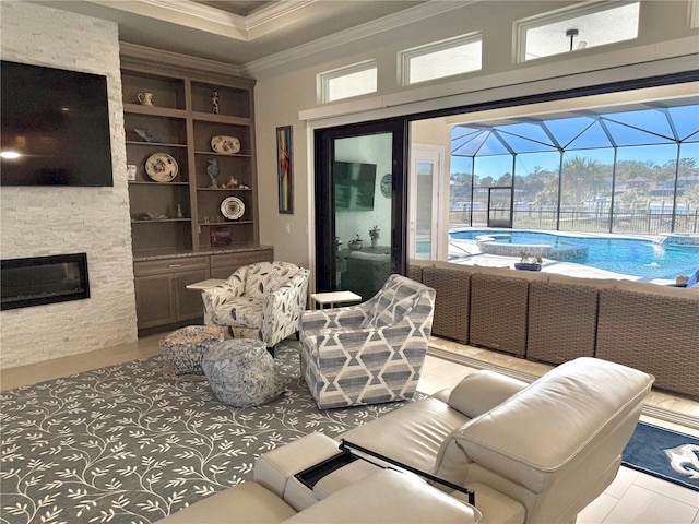 living area featuring a stone fireplace, built in shelves, crown molding, and a sunroom