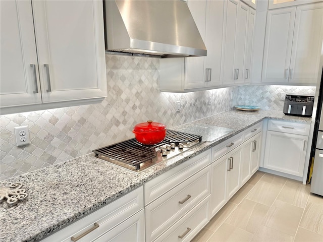 kitchen with light stone counters, backsplash, white cabinets, wall chimney range hood, and stainless steel gas cooktop