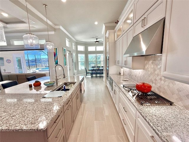 kitchen with under cabinet range hood, a sink, tasteful backsplash, stainless steel gas stovetop, and glass insert cabinets