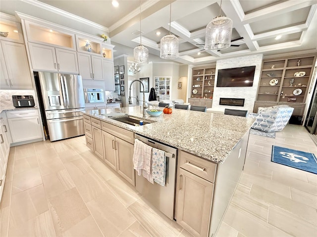 kitchen with a sink, a large fireplace, appliances with stainless steel finishes, coffered ceiling, and a kitchen island with sink