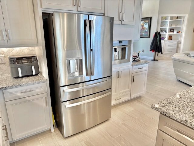 kitchen with tasteful backsplash, appliances with stainless steel finishes, and light stone countertops