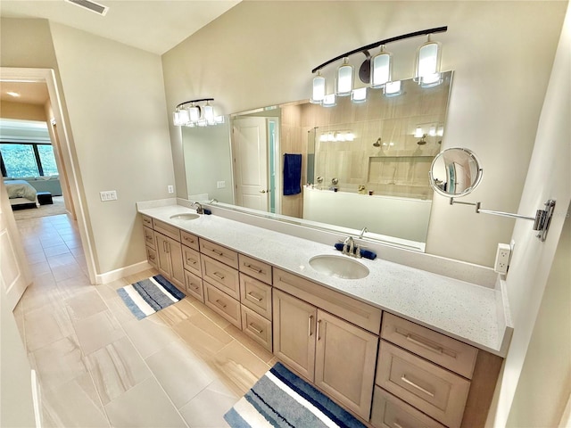 ensuite bathroom with double vanity, connected bathroom, a walk in shower, and a sink