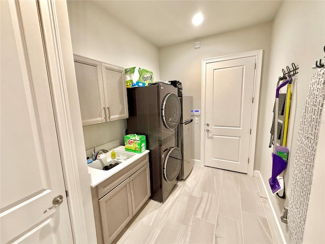 clothes washing area with stacked washing maching and dryer, cabinet space, baseboards, and a sink