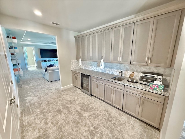 kitchen featuring visible vents, a toaster, a sink, wine cooler, and light colored carpet