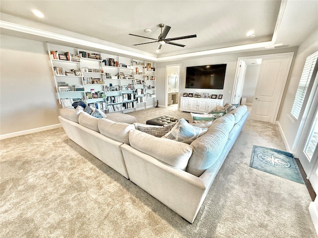 carpeted living room with a tray ceiling, a ceiling fan, and baseboards