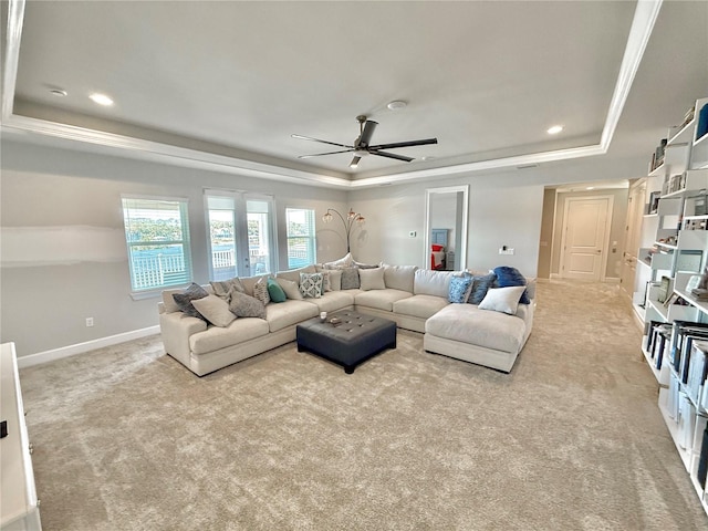 living area featuring a raised ceiling, carpet, crown molding, baseboards, and ceiling fan