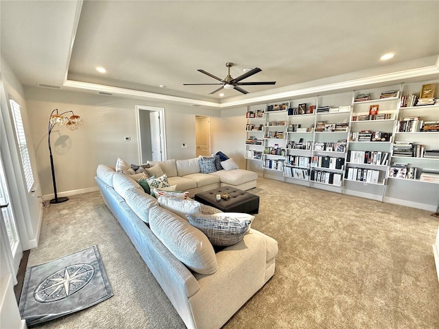 living area featuring a raised ceiling, carpet, and ceiling fan