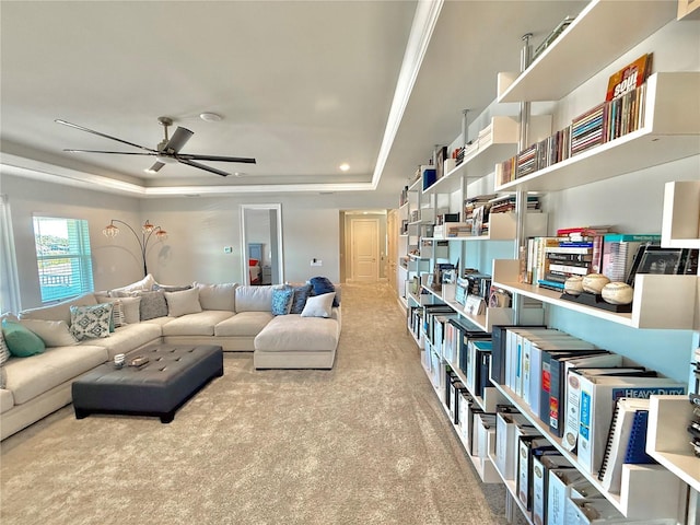 living area featuring a ceiling fan, a raised ceiling, carpet, and ornamental molding