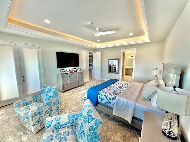 bedroom with a raised ceiling, recessed lighting, ensuite bathroom, and light carpet