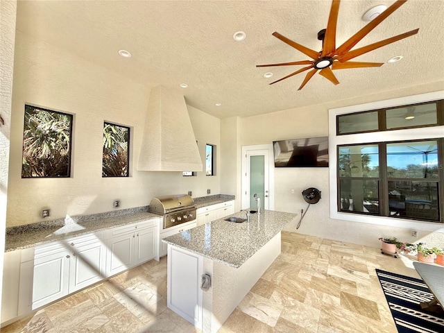 kitchen featuring light stone counters, white cabinets, a textured ceiling, and a healthy amount of sunlight