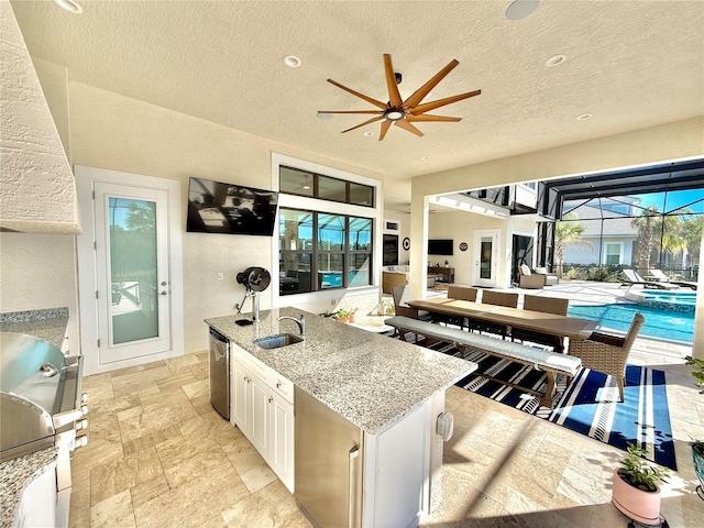 kitchen featuring a sink, light stone countertops, stainless steel dishwasher, white cabinetry, and a kitchen island with sink