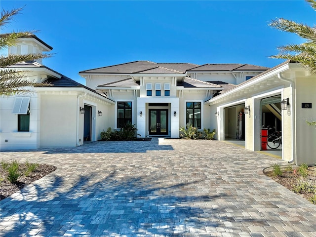 view of front of property with french doors, decorative driveway, an attached garage, and stucco siding