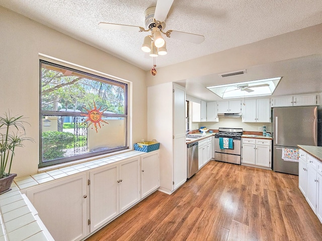 83 Farragut Dr, Palm Coast, FL 32137 - kitchen with stainless steel appliances, tile countertops, light wood-style floors, a textured ceiling, and a skylight