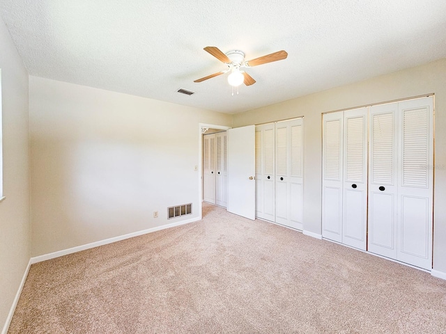 83 Farragut Dr, Palm Coast, FL 32137 - unfurnished bedroom with light carpet, multiple closets, a textured ceiling, and a ceiling fan