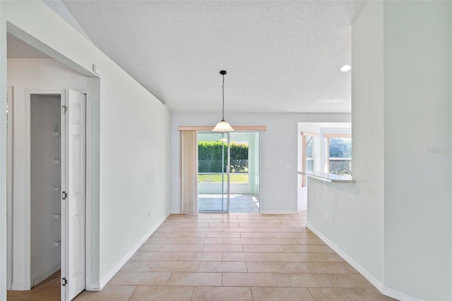 unfurnished dining area featuring light tile patterned flooring, a textured ceiling, and baseboards