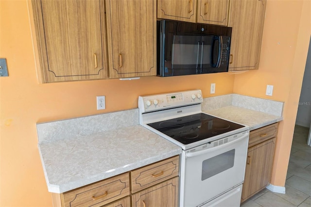 kitchen featuring black microwave, light countertops, light tile patterned floors, brown cabinets, and white range with electric stovetop