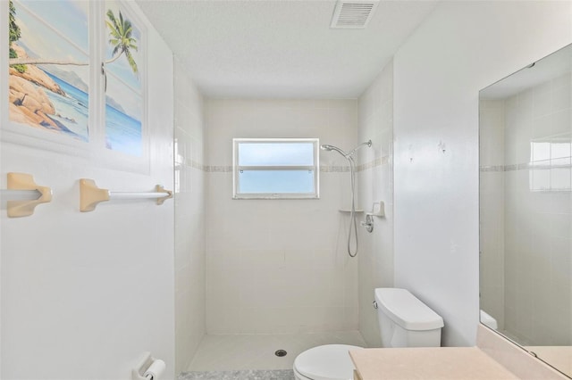 bathroom featuring visible vents, toilet, vanity, tiled shower, and a textured ceiling