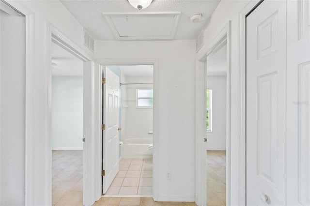 hall with attic access, light tile patterned flooring, visible vents, and a textured ceiling