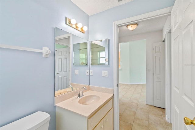 half bathroom featuring tile patterned flooring, a textured ceiling, toilet, and vanity