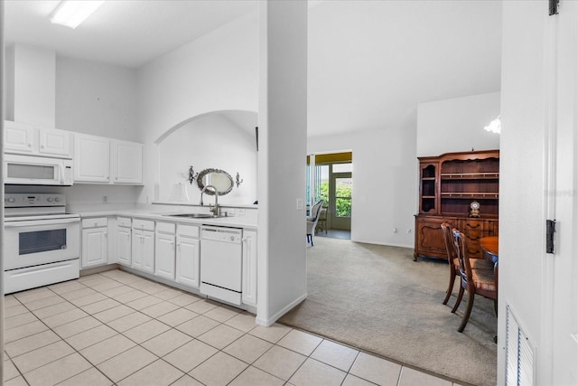 kitchen featuring a sink, white appliances, light countertops, light colored carpet, and a towering ceiling