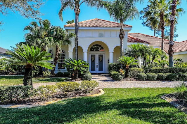 mediterranean / spanish-style house featuring a tiled roof, french doors, a front yard, and stucco siding