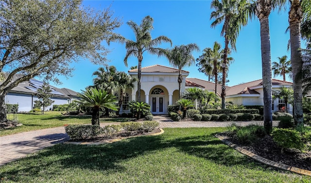 mediterranean / spanish-style house featuring a tiled roof, french doors, a front lawn, and stucco siding