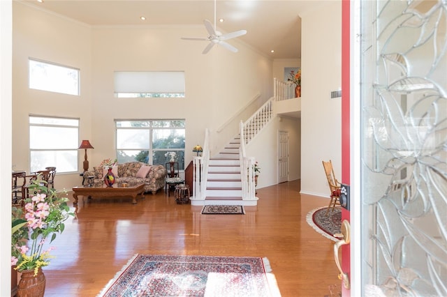 foyer featuring stairs, ornamental molding, a high ceiling, wood finished floors, and a ceiling fan