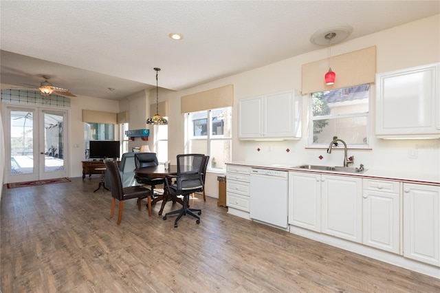 kitchen featuring pendant lighting, light wood-style flooring, a sink, white cabinets, and white dishwasher